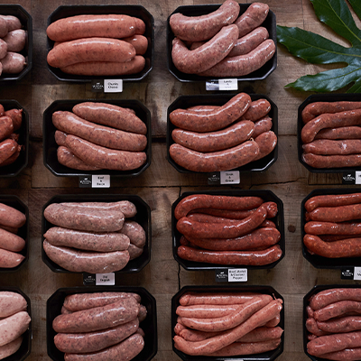 Overview of various sausage flavours packed in trays with a leaf garnish in the top right corner.