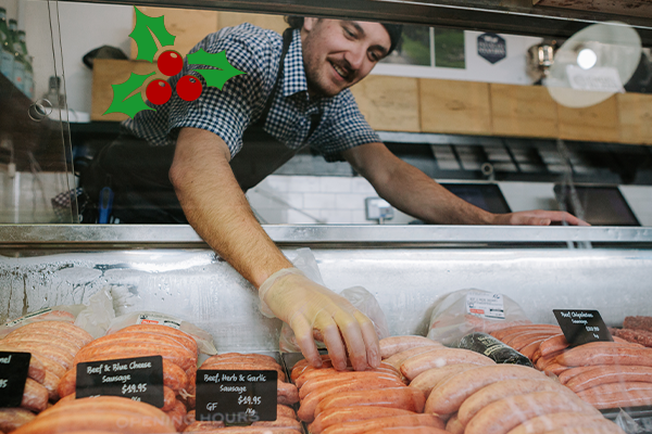 Waipawa Butcher Rhys Tamanui stands behind a glass cabinet filled with sausages, he is placing sausages in a row.