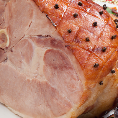 A baked Ham dressed with cloves sits on a christmas themed table.