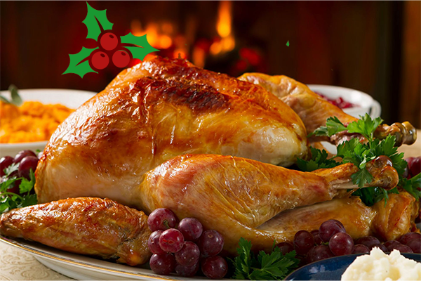 A golden dressed turkey sits on a white plate surrounded by garnishes. In the background you can see a roaring fire.