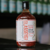 Waipawa Butchery Glasseye meat sauce sitting on a reflective bench top with out of focus bottles behind it.