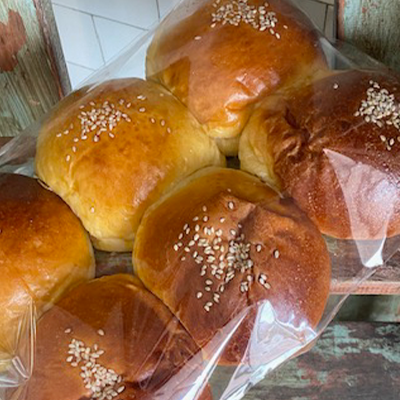 Six golden potato rolls with sesame seeds on top, are wrapped in plastic, and sitting on top of an old wooden ladder.