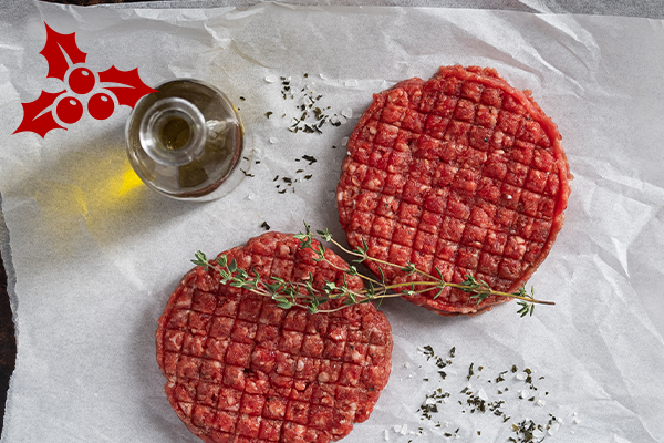 Overview shot of two raw beef burger patties sitting on wax paper. A sprig of thyme sits on top.