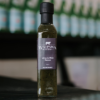 A bottle of Waipawa Butchery lime and mint sauce sits on a reflective bench with out of focus bottles behind it.