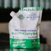 A pouch of little bone broth green Thai curry sits on a reflective bench with out of focus bottles behind it.