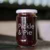 A jar of Pickle and Pie Cranberry Chutney sits on a reflective bench with out of focus bottles behind it.