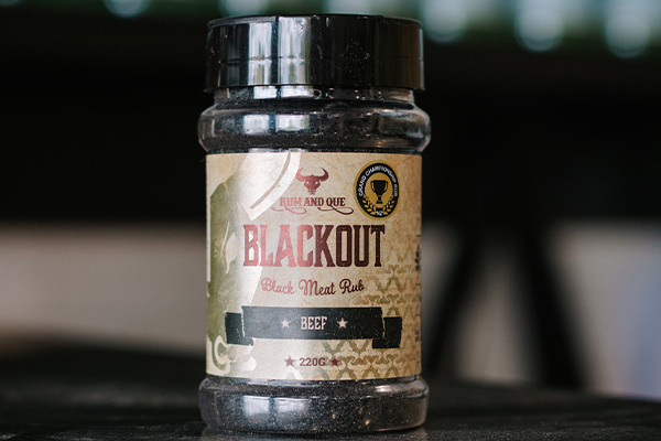 A shaker of Rum and Que Blackout Rub sits on a reflective bench.