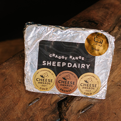 A wrapped packet of Craggy Range Sheep Dairy Blue cheese sits on a wooden board.