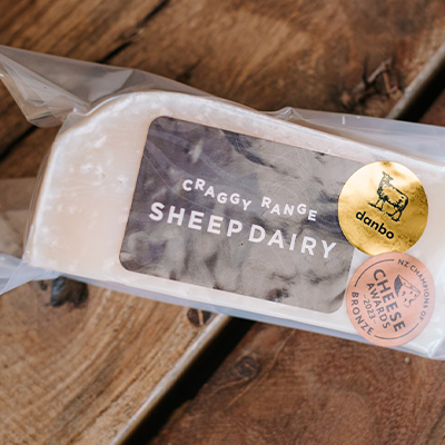 A wrapped packet of Craggy Range Sheep Dairy Danbo cheese sits on a wooden board.