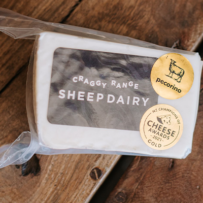 A wrapped packet of Craggy Range Sheep Dairy Pecorino cheese sits on a wooden board.