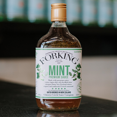 A bottle of Glasseye Creek's forking mint premium sauce sits on a bench with a blurred background.